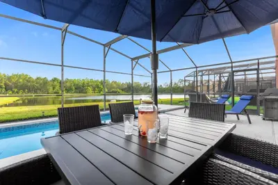a table with an umbrella and a drink on it at Lake View Vacation Home with Pool and Game Room Near Disney Parks in Kissimmee