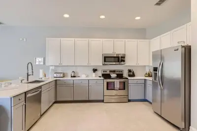 a kitchen with white cabinets and a stainless steel refrigerator at The Marvel Mansion 5BR Pool Home Near Disney World in Orlando