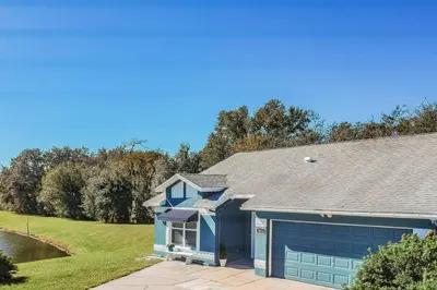 a blue house with a garage and a pond at THIS IS PARADISE FOUND! Private In-Ground Pool Home, Views, Near Dis, NO Steps, LOW Rates! in Kissimmee