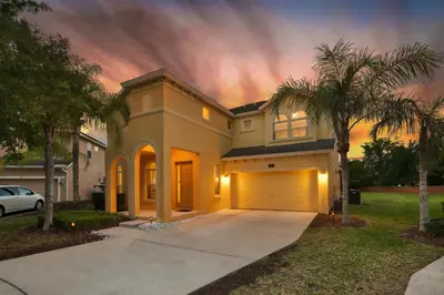 a house with a garage and a palm tree at Family Retreat 6BR Villa with Private Pool, Spa & Theater near Disney in Kissimmee
