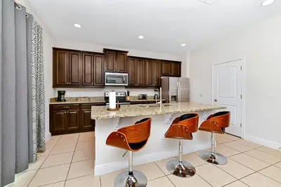 a kitchen with brown cabinets and a counter with bar stools at Enchanting Home Near Disney With Game And Themed Rooms With Waterpark & Resort Access At Encore Resorts Reunion - 7403Mr in Kissimmee