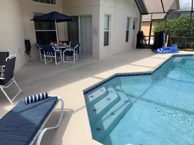 a swimming pool with a table and an umbrella at Emerald Escape - New Pool Home in Kissimmee