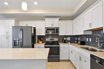 a kitchen with white cabinets and a stainless steel refrigerator at Cozy Condo Only 6 Minutes From Disney World in Kissimmee