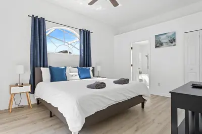 a white bedroom with a large bed with blue pillows at Amazing Pool Spacious 3BR House near Disney in Kissimmee