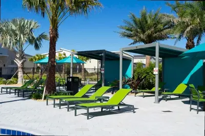 a group of lounge chairs and umbrellas next to a pool at Splendid 5Bd Close to Disney at Storey Lake 4251 in Kissimmee