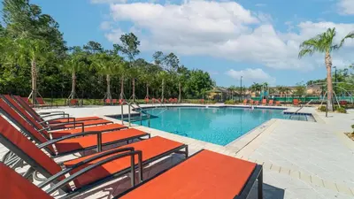 a swimming pool with red chairs and trees at 4543 Narrative in Kissimmee