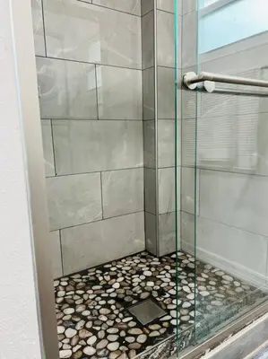 a shower with a glass door and a pebble floor at Roy's guest house in Orlando