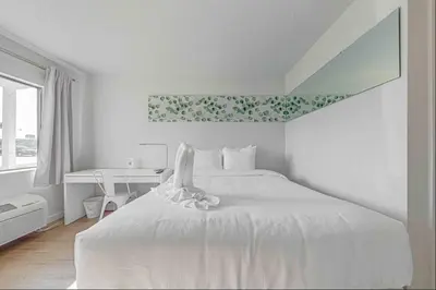 a white bedroom with a white bed and a desk at Travel Lodge by Wyndham 10 min from Disney in Kissimmee