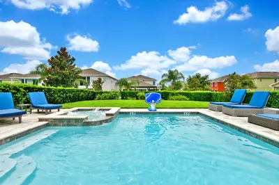 a swimming pool with blue chairs and a blue umbrella at Elegant Home With Private Pool, Waterpark & Resort Access Near Disney At Encore Resort - 7610Wi in Kissimmee