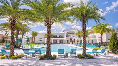 a resort swimming pool with palm trees and blue chairs at Mario 12BR Villa w/ Private Green View Pool in Kissimmee