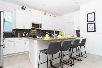 a kitchen with white cabinets and a bar with stools at Spacious & Comfy Retreat Prime Location Amazing in Kissimmee