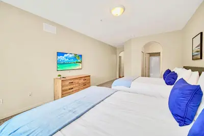 two beds in a bedroom with white walls and blue pillows at Near Disney - 2BR Condo Unit - Pool in Orlando