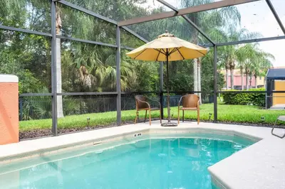 a pool with an umbrella and two chairs and a table with an umbrella at Spectacular House with 3BR - Private Pool, BBQ - Minutes from Disney! in Kissimmee