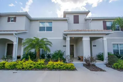 a large white house with a palm tree at Prime Locale - Vacation Paradise in Kissimmee