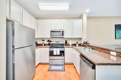 a kitchen with white cabinets and a stainless steel refrigerator at Modern 2BR Condo - Pool - Near Disney in Orlando