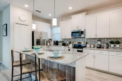 a kitchen with white cabinets and a island with chairs at Luxury 5BR Home, Private Pool, Prime Location in Kissimmee