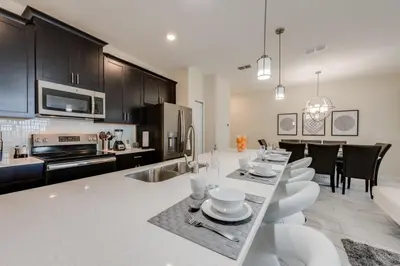 a kitchen with black cabinets and a table with white chairs at Cozy Home Prime Disney Parks Location in Kissimmee