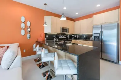 a kitchen with orange walls and a large island with white chairs at Spacious Comfortable Perfect Vacation in Orlando