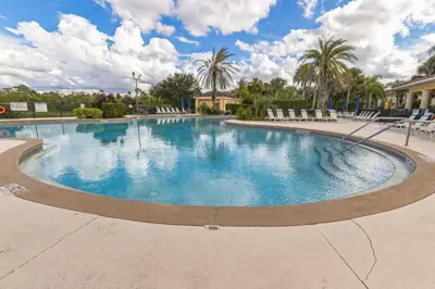 a large swimming pool with chairs and palm trees at Amazing Disney Themed Oasis 3BR near Parks townhouse in Orlando