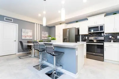 a kitchen with white cabinets and a island with bar stools at 3BR Resort Condo FREE Waterpark 3150 in Kissimmee