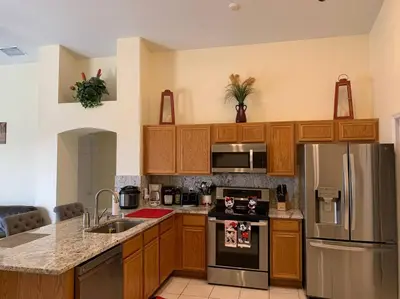 a kitchen with wooden cabinets and a stainless steel refrigerator at Minutes to Disney! Spacious Home w/ Private Pool, Themed Rooms! in Orlando