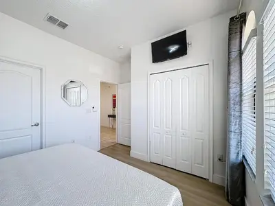 a bedroom with a white bed and a tv on the wall at Tranquility Hut, Spacious 4-bedrooms, 4-bathrooms, Pools, free parking in Kissimmee