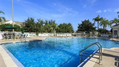a large blue swimming pool with chairs and umbrellas at Immaculate 4 bedrooms 3 bathroom in Windsor Palms in Kissimmee