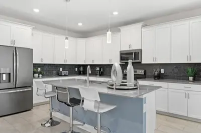 a kitchen with white cabinets and a large island with bar chairs at Relax & Unwind Chic Pool Home Near Disney Fun! - STL113 in Kissimmee