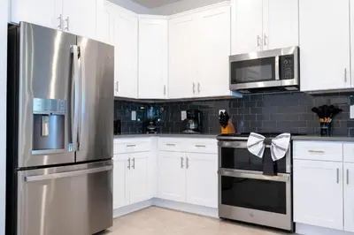 a kitchen with white cabinets and a stainless steel refrigerator at Last Minute Disney Private Pool Hot Tub Game Room Themed Bedrooms. Book Now 90505 in Kissimmee