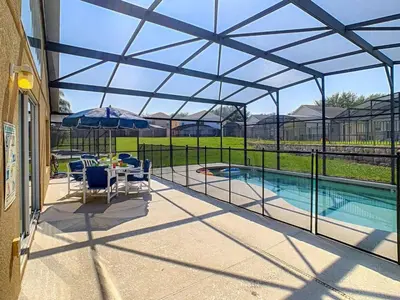 a screened in pool with a table and chairs and an umbrella at H8536 Single Level Pool Spa Home 5 Bed Near Disney in Kissimmee