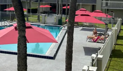 a pool with red umbrellas and a man sitting in a chair next to at Bposhtels Orlando Disney in Kissimmee