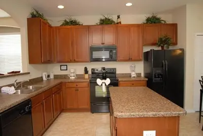 a kitchen with wooden cabinets and a black refrigerator at Beautiful Renovated 6 Bed Pool Home home in Kissimmee