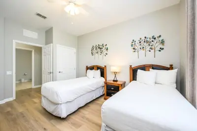 two beds in a bedroom with white walls and wood floors at Vista Cay Deluxe Condo, Near The Parks! - 3002 in Orlando