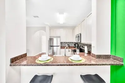 a kitchen with white cabinets and a counter with chairs at Modern 3BR Condo Near Disney- Pool in Orlando
