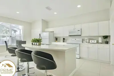 a white kitchen with white cabinets and black chairs at Renewed & Cozy 4BD Great Location near Disney in Kissimmee