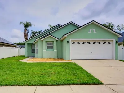 a green house with a white garage at Pool home 5 miles to Disney Great for families in Orlando