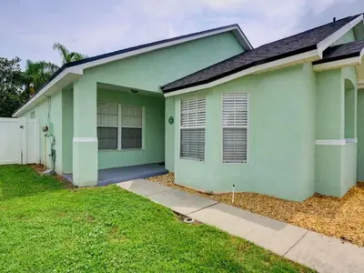 a green house with a sidewalk in front of it at Pool home 5 miles to Disney Great for families in Orlando