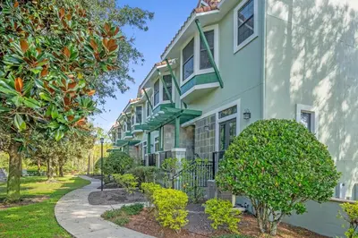 a building with green trim and trees next to a sidewalk at Sunny Stay in FL - 4-Bedroom Townhome by Disney! in Orlando