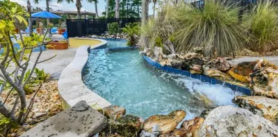 a pool with a waterfall in a backyard with rocks at 201 HB - Hideaway at TerraVerde in Kissimmee