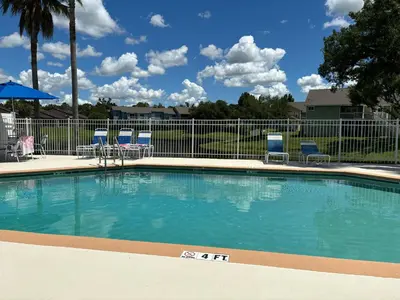 a large swimming pool with chairs and a fence at Spacious Condo Close to Disney Attractions in Kissimmee