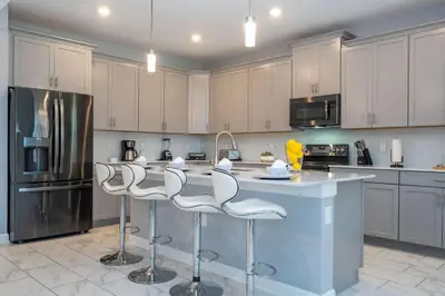 a kitchen with white cabinets and a island with bar stools at Luxury 6BR Resort Home - Pool, Hot Tub & BBQ - Near Disney! in Kissimmee
