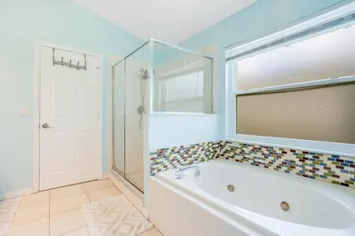 a bathroom with a tub and a shower and a mirror at Relaxing Retreat with Pool and Movie Theater in Orlando