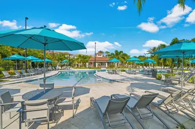a pool with tables and chairs and blue umbrellas at Modern Resort 2BR near Icon park, Convention center and NEW Epic Universe in Orlando