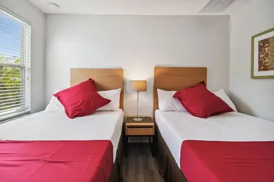 two beds with red pillows in a room at 2 Suítes c/ Jacuzzi • 10min da Disney in Kissimmee