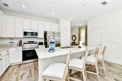 a kitchen with white cabinets and a kitchen island with chairs at Breezy Blue Villa Near Disney With Margaritaville Resort Access - 3120Cs in Orlando