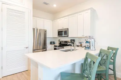 a kitchen with white cabinets and a counter with chairs at Peachside Cottage Near Disney With Margaritaville Resort & Island H2O Access - 8037Dr in Orlando