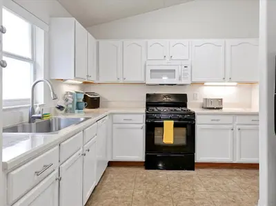 a kitchen with white cabinets and a black stove at 6BD - Pool, BBQ & Movie Theater - 10 Mins to Disney in Kissimmee