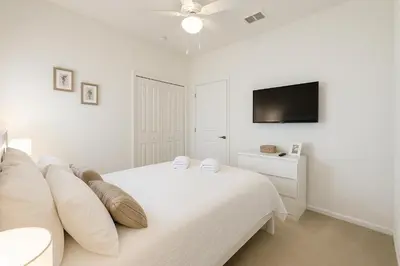a white bedroom with a bed and a flat screen tv at 2612 LunaPi Villa 7Bd Private Pool and Family Room in Kissimmee