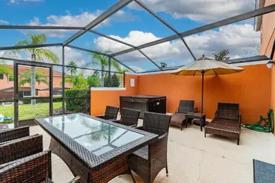 a patio with a glass table and chairs and an umbrella at Casa 3Q Resort + Jacuzzi Perto Disney in Kissimmee