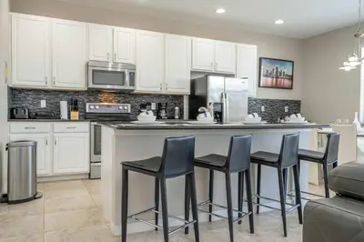a kitchen with white cabinets and a bar with stools at 4BR Lakefront - Themed Rooms - Pool & BBQ! in Kissimmee